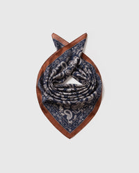 Silk paisley scarf coiled to show the soft drape and the cognac border catching the light