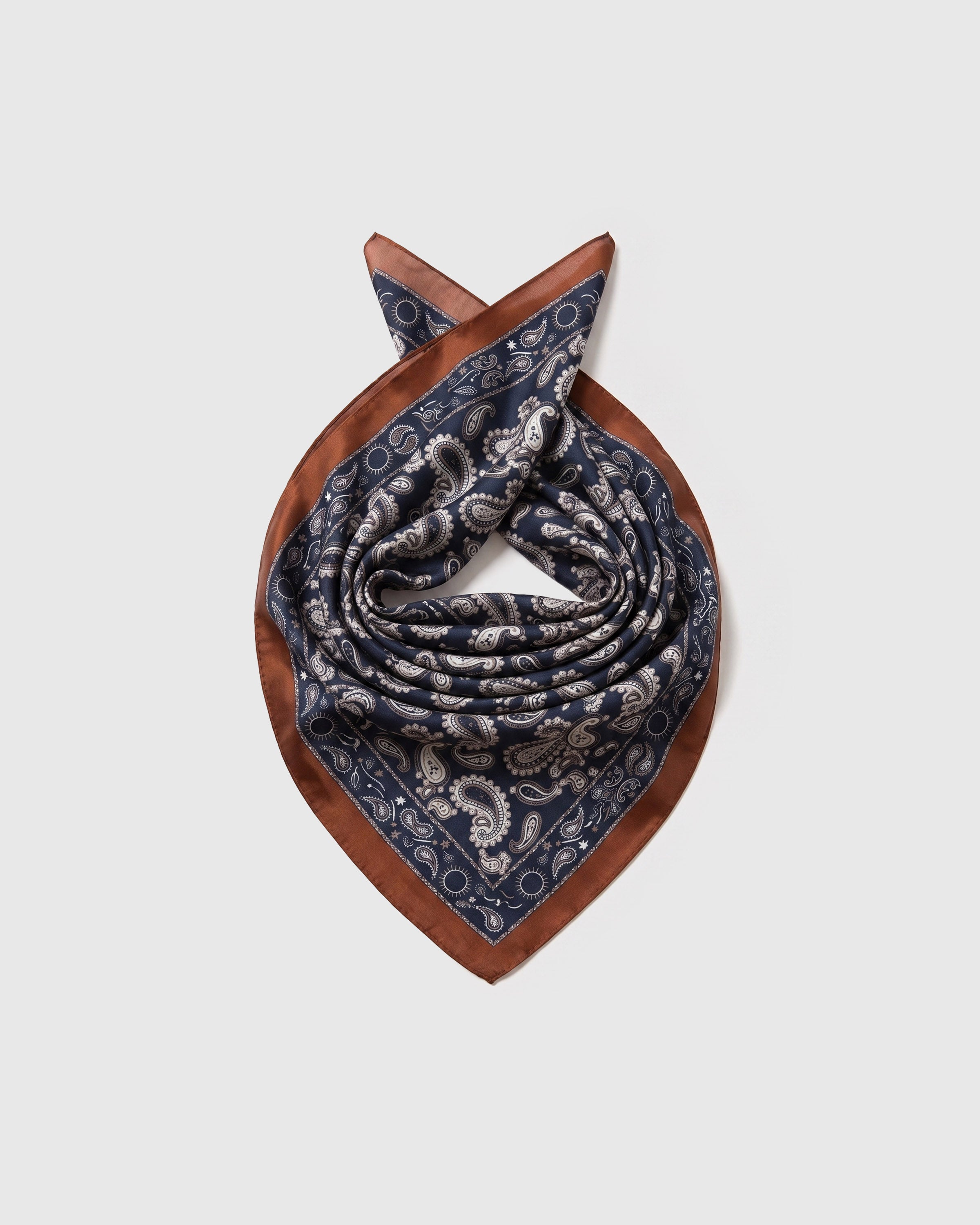 Silk paisley scarf coiled to show the soft drape and the cognac border catching the light