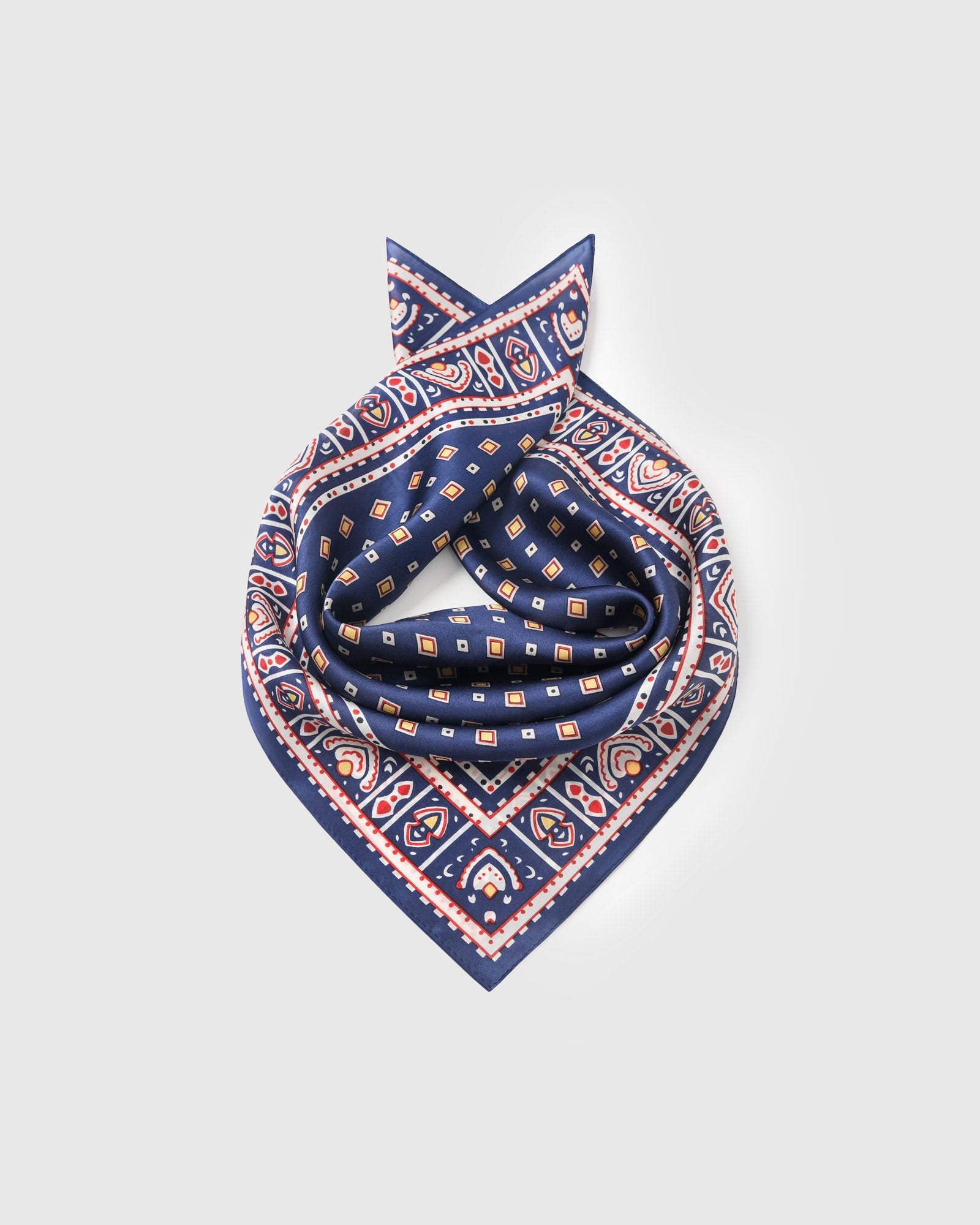 Silk foulard scarf coiled to show the drape of pure silk and the mustard diamond motif