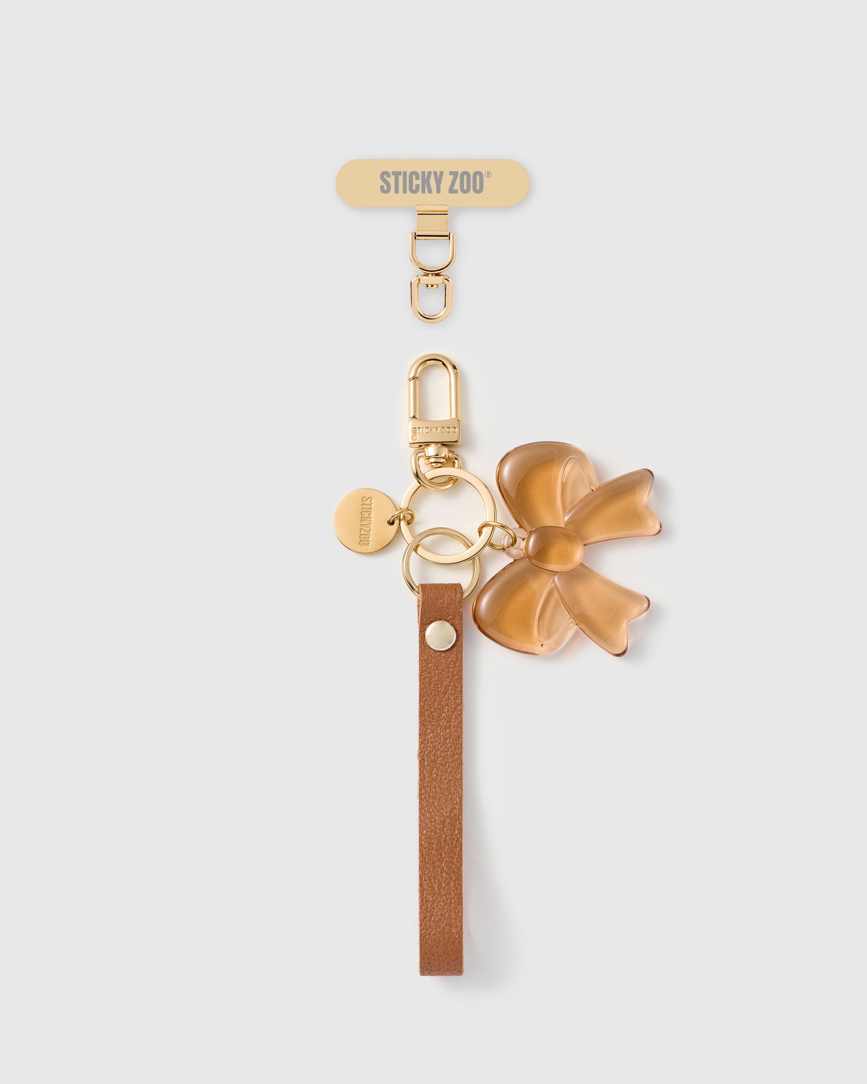 Handmade French Alran cocoa tan leather phone strap with translucent amber resin bow charm and 18K gold STICKYZOO hardware