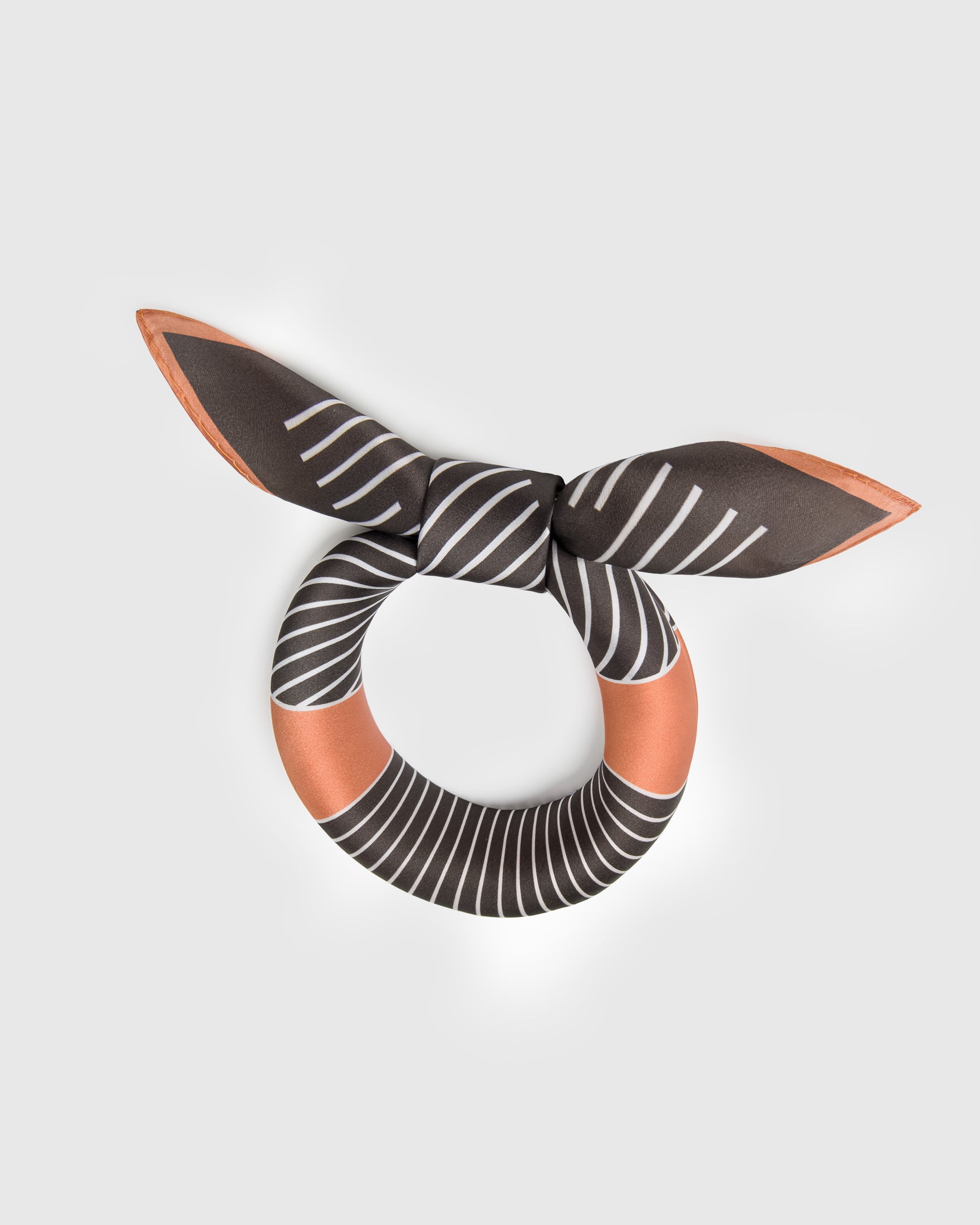 Silk op-art scarf folded into a ribbon shape showing the soft drape of pure silk and the terracotta border