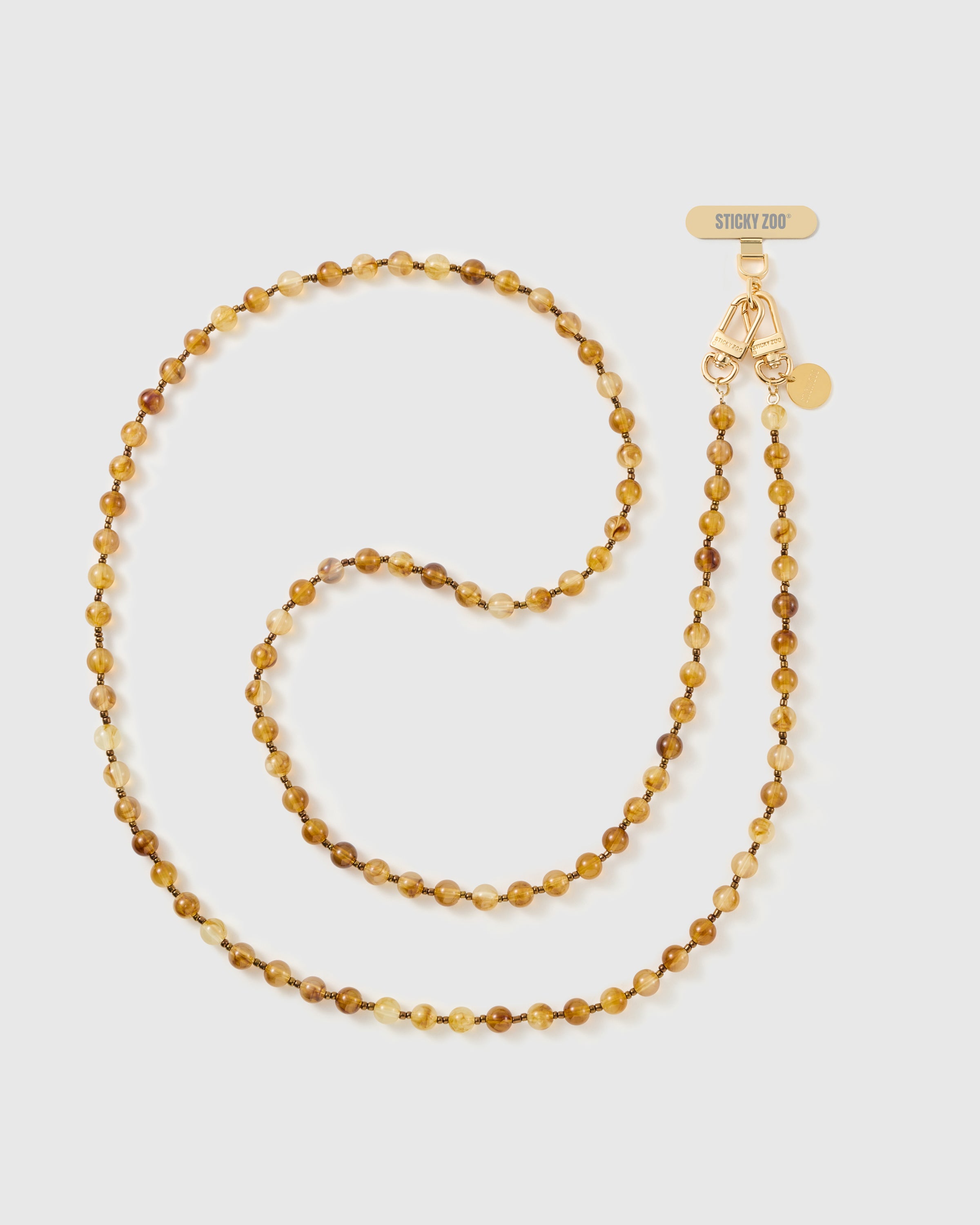 Full-length STICKYZOO crossbody phone strap of translucent amber and honey resin beads with bronze spacers, coiled beside a gold-tone dual clasp.