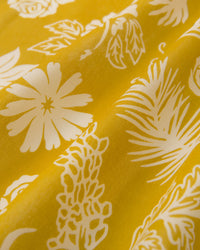 Close-up of hand-illustrated daisies, palms and ferns printed in ivory on the mustard silk field
```