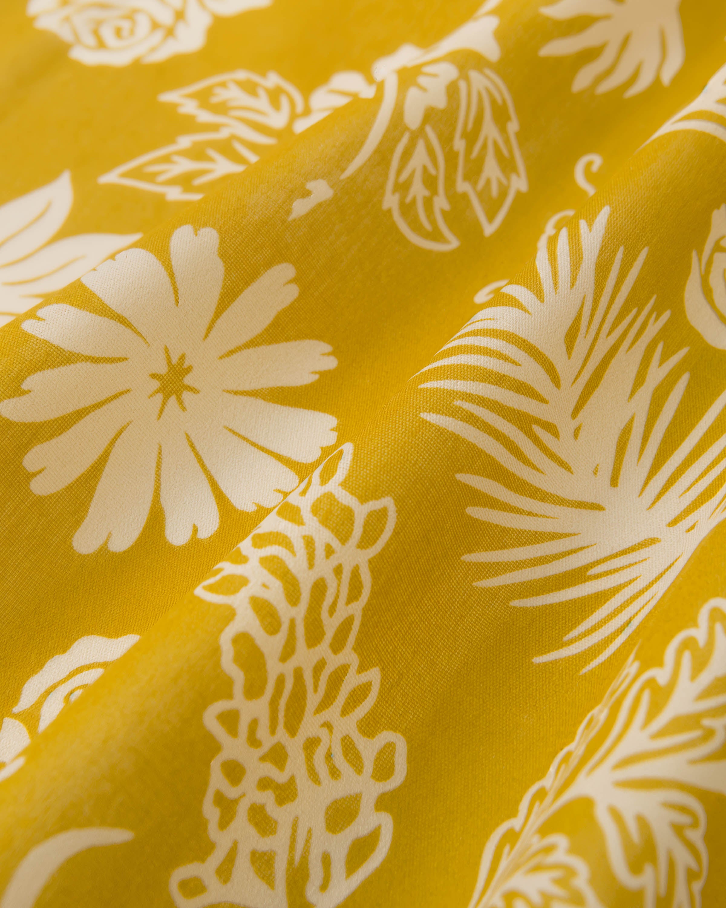 Close-up of hand-illustrated daisies, palms and ferns printed in ivory on the mustard silk field
```