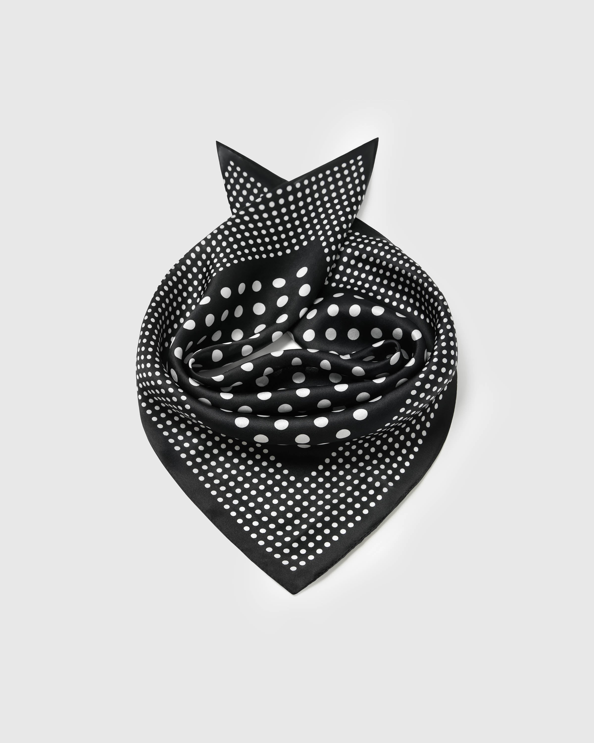 Black silk polka dot scarf coiled into a soft bandana fold showing both dot scales