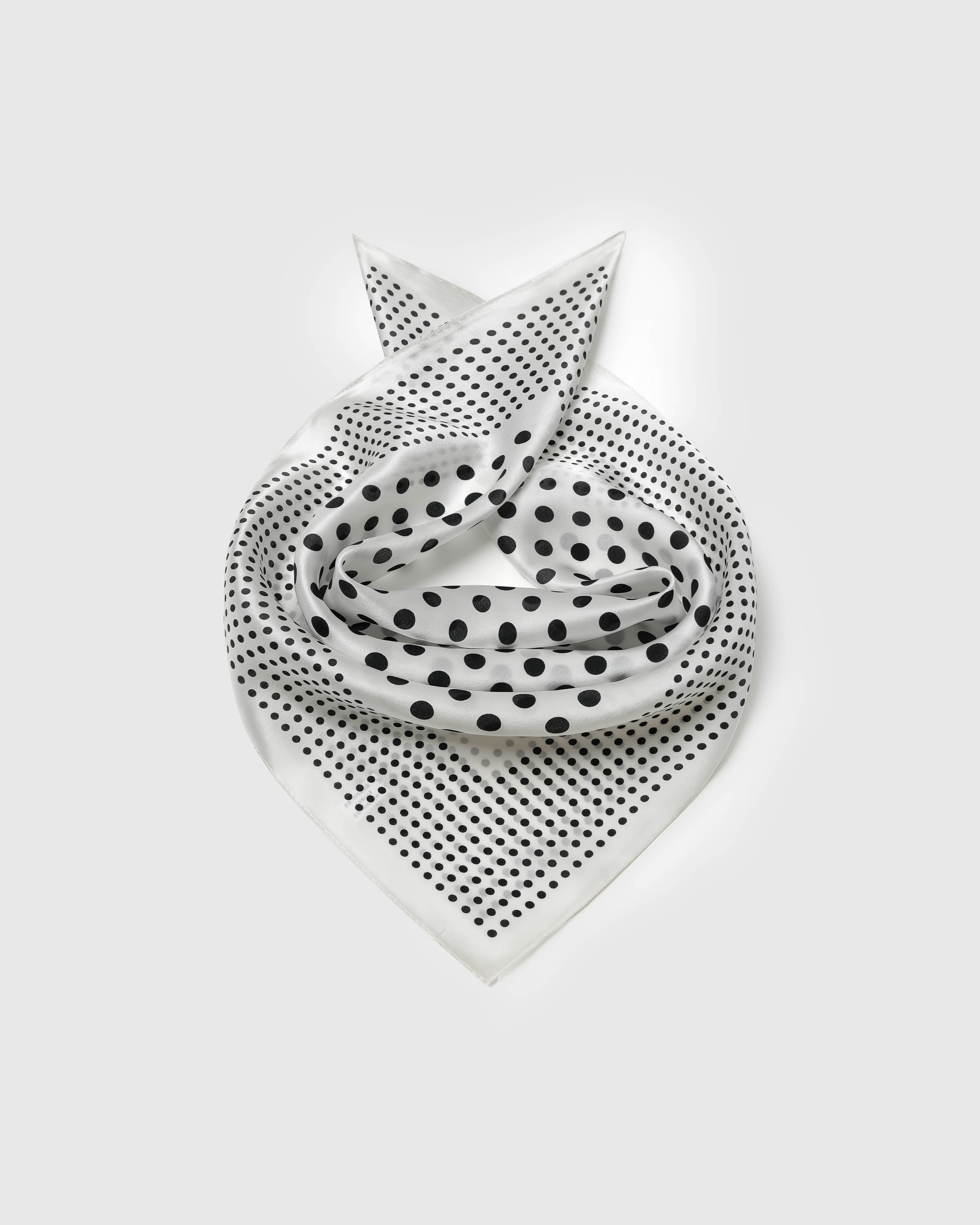 Ivory silk polka dot scarf coiled into a soft bandana fold showing both dot scales across the field