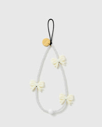 STICKYZOO ivory bow phone strap laid flat, a loop of white faux-pearl beads with three glossy ivory bows, a black cord loop and gold disc
