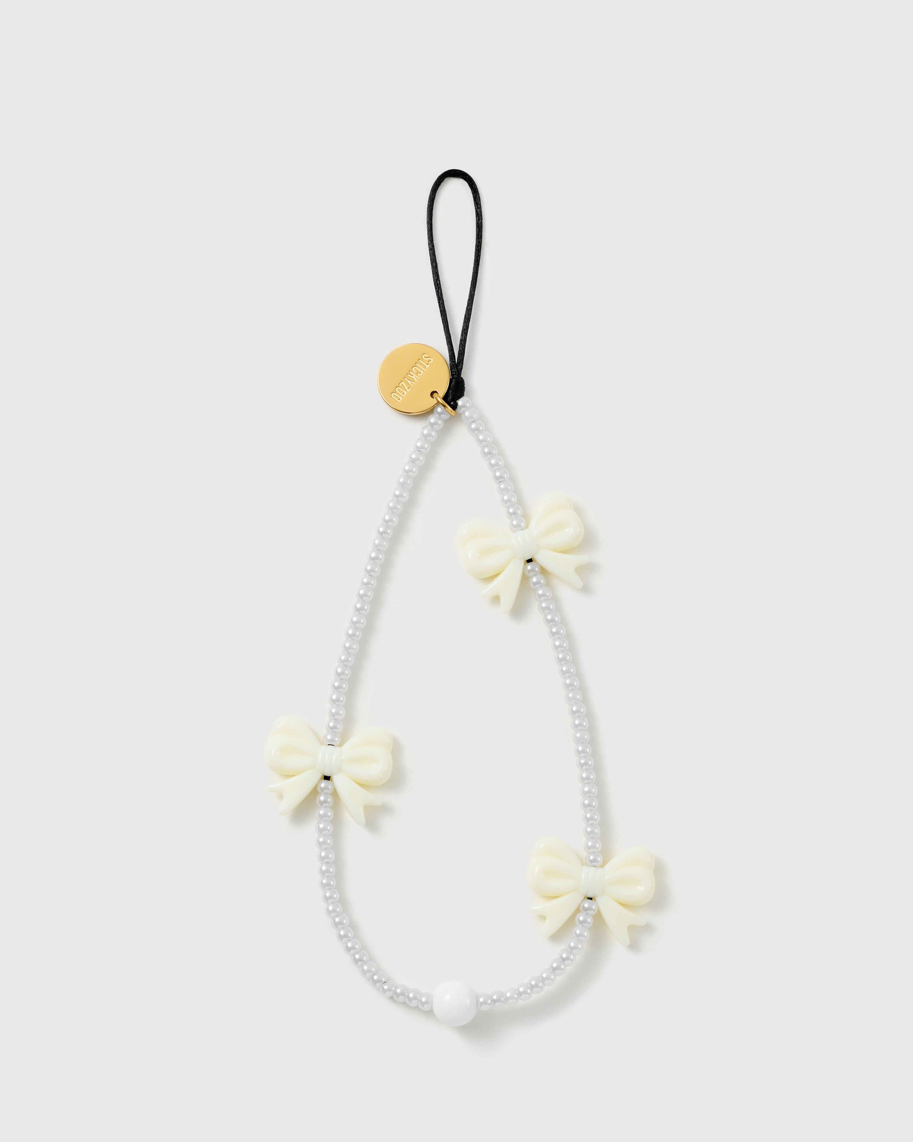 STICKYZOO ivory bow phone strap laid flat, a loop of white faux-pearl beads with three glossy ivory bows, a black cord loop and gold disc
