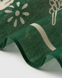 Close-up of the forest-green silk scarf coiled to show the soft drape and ivory daisy silhouette
