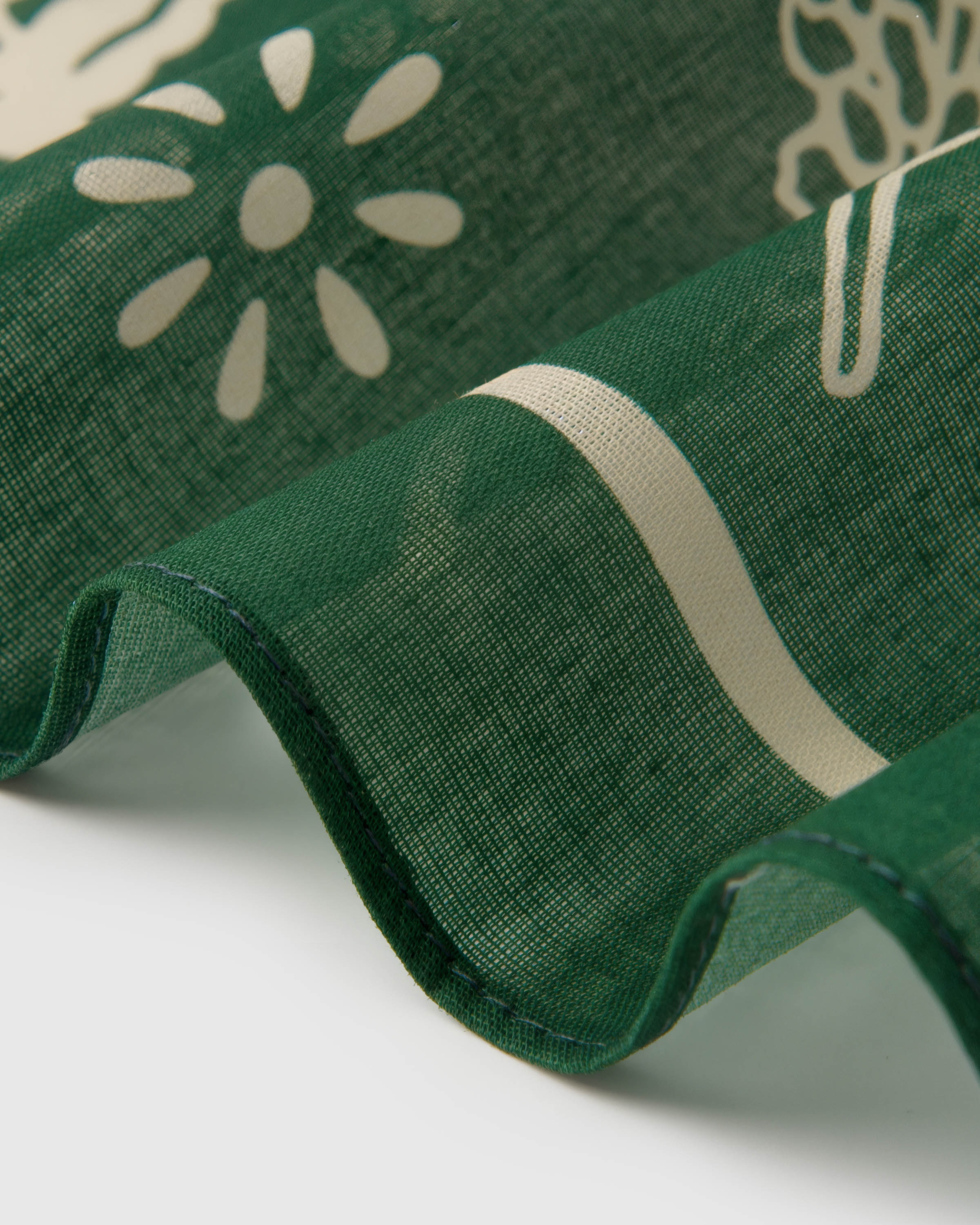 Close-up of the forest-green silk scarf coiled to show the soft drape and ivory daisy silhouette