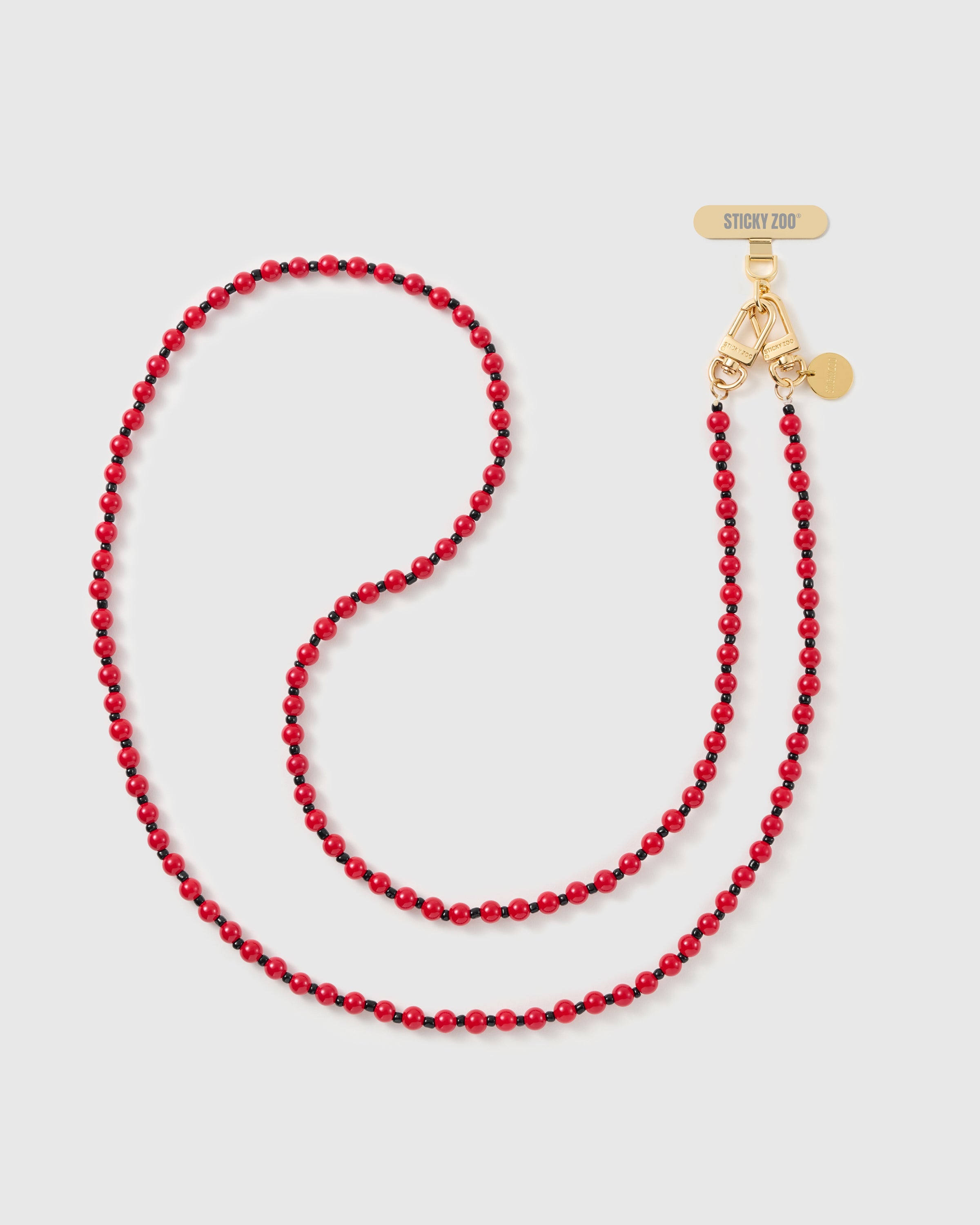 STICKYZOO cross-body phone strap in glossy scarlet beads with black spacers, laid in an S-curve with a gold-tone dual clasp and engraved tag.