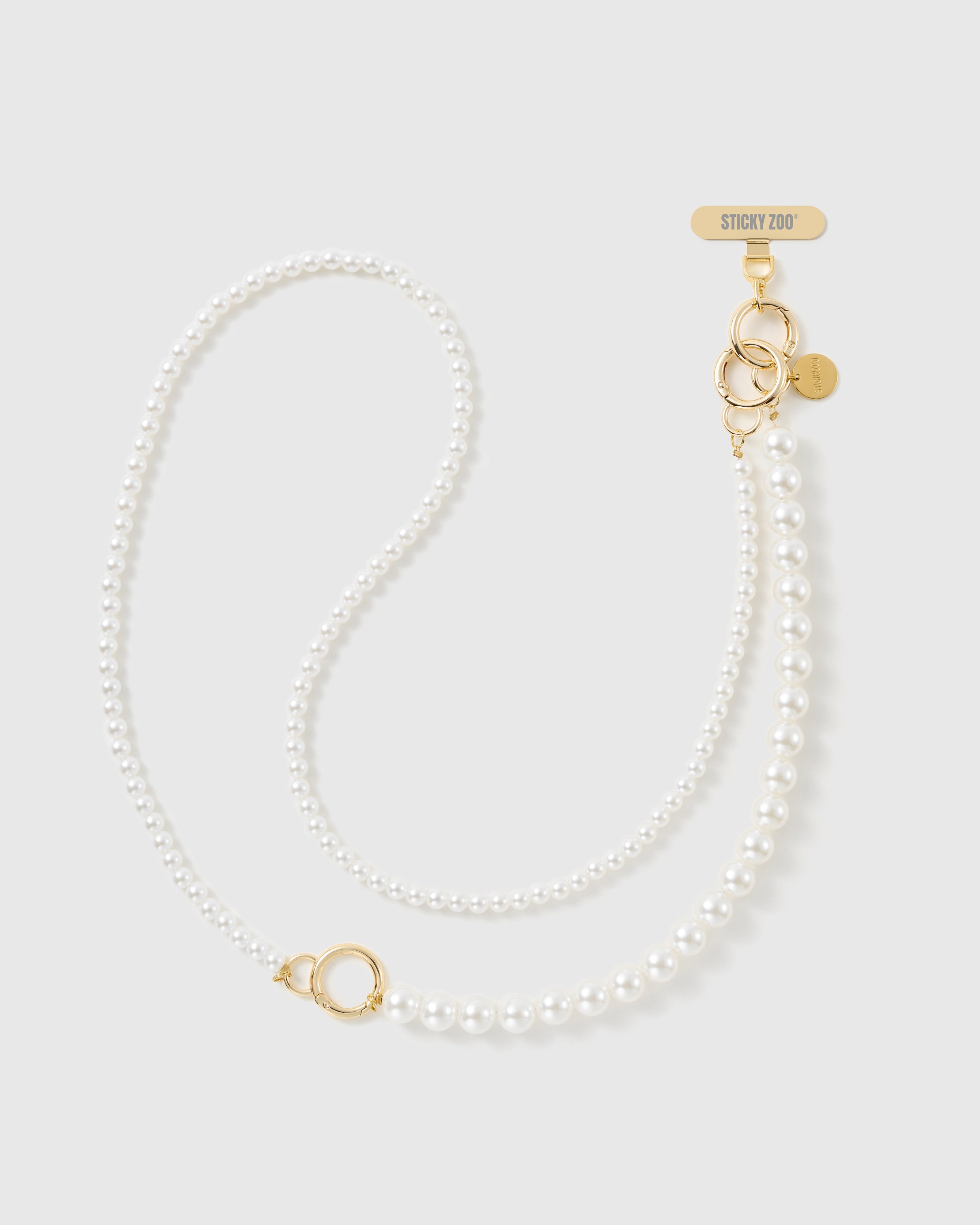 STICKYZOO two-size faux-pearl cross-body phone strap laid in an S-curve, small round pearls flowing into larger ones with a gold-tone ring and clasp