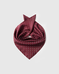 Burgundy foulard silk scarf coiled to show the silver floret grid and the small-square format