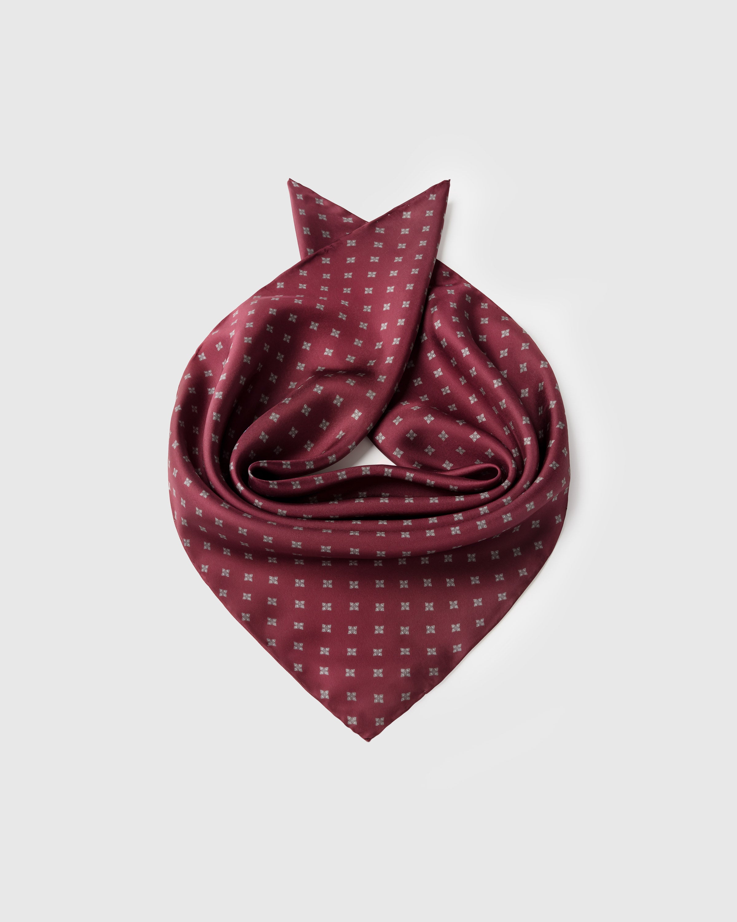 Burgundy foulard silk scarf coiled to show the silver floret grid and the small-square format