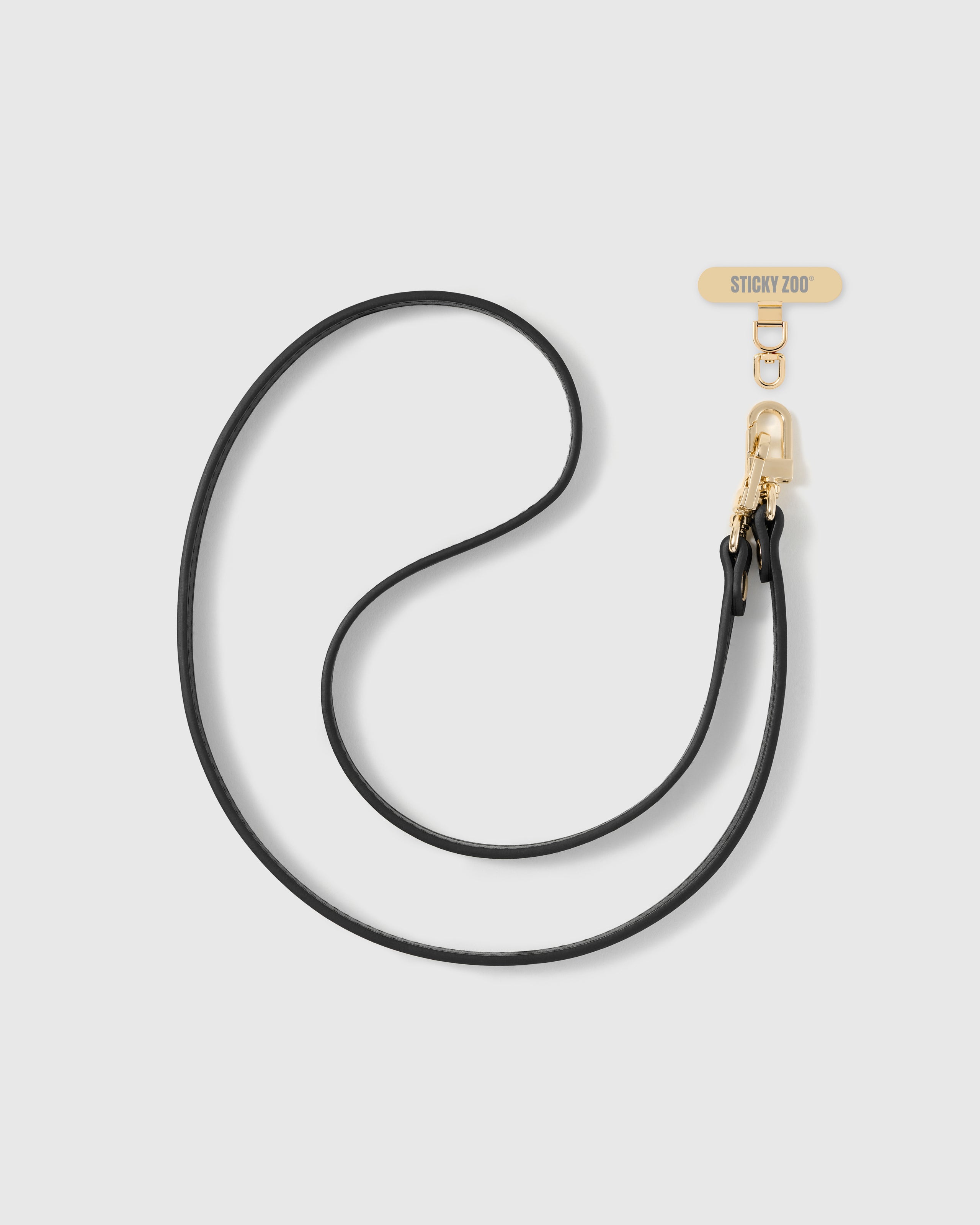 STICKYZOO black vegan-leather cross-body phone strap shown in full with stitched edging, warm gold hardware and a Phone Strap Card