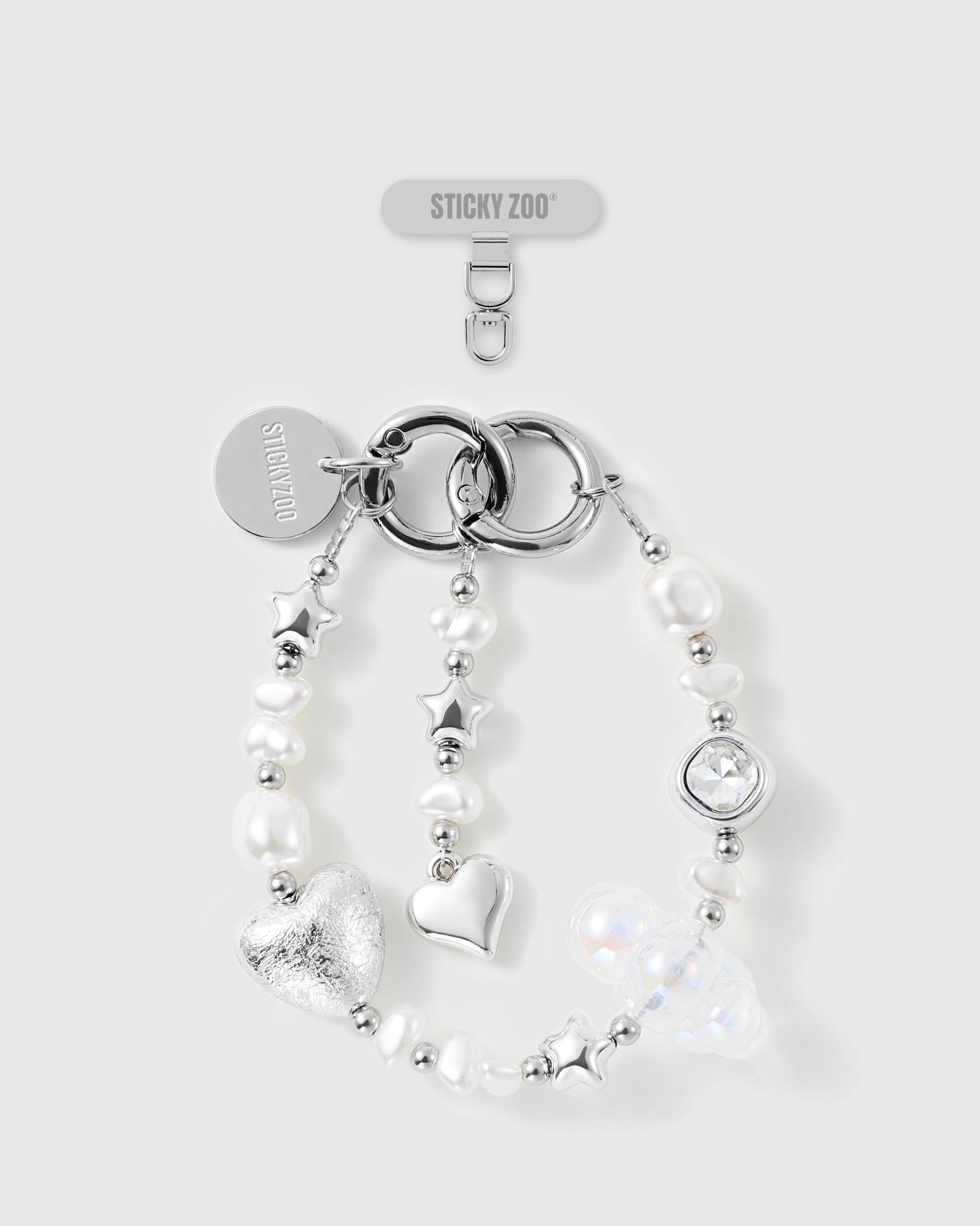 STICKYZOO beaded phone strap flat-lay: white pearl-effect beads, silver-tone stars, foil-textured heart, clear faceted gem, hook, card and disc