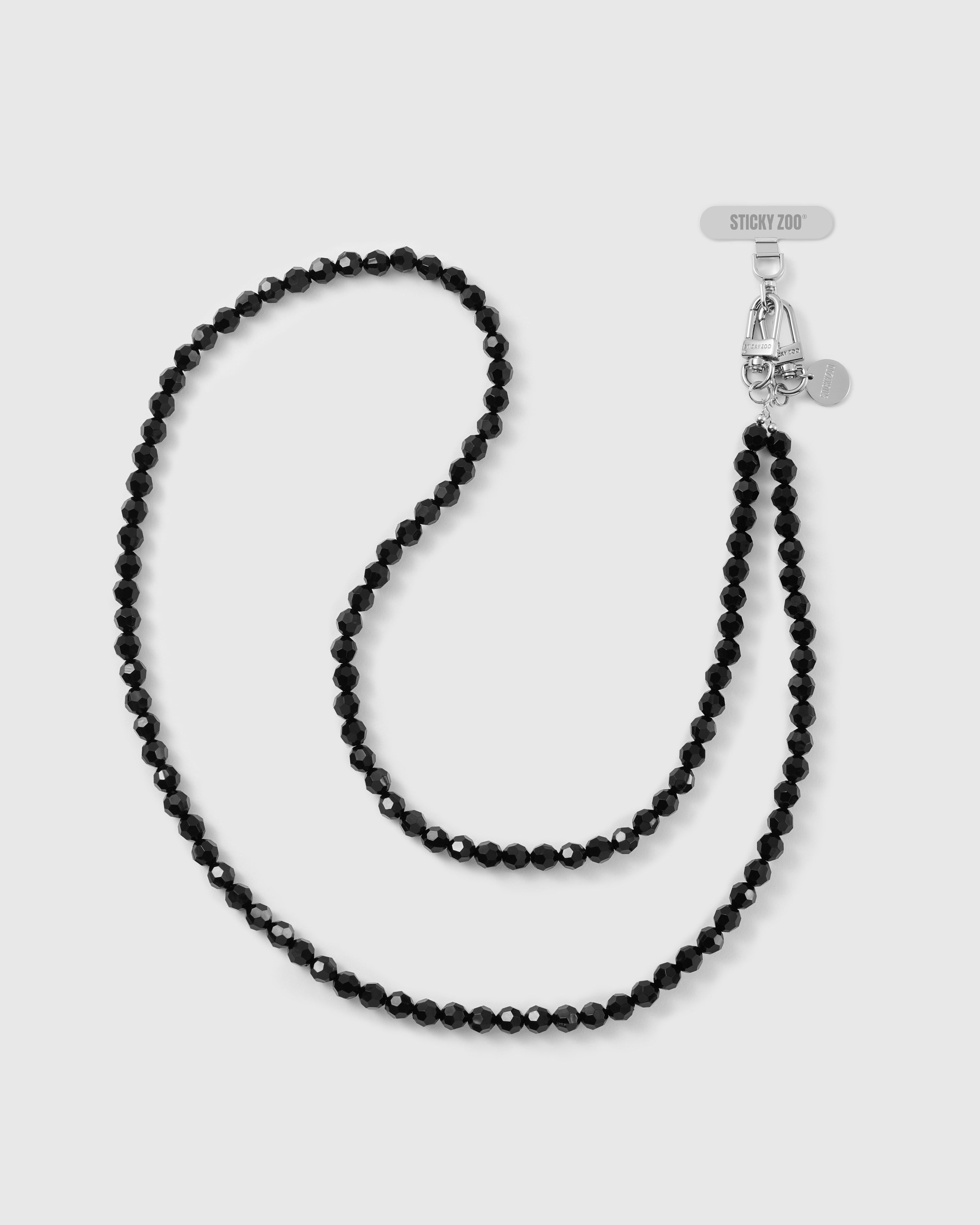 STICKYZOO faceted jet-black beaded cross-body phone strap laid in an S-curve, silver-tone dual clasp and engraved disc at the top.