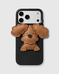 STICKYZOO Poodle Puppy Charm Case — handmade 3D leather poodle charm in warm brown with curly floppy ears and black nose on textured black leather phone case. Hand-cut, stitched, and layered from French Alran leather. Rated 4.9★.