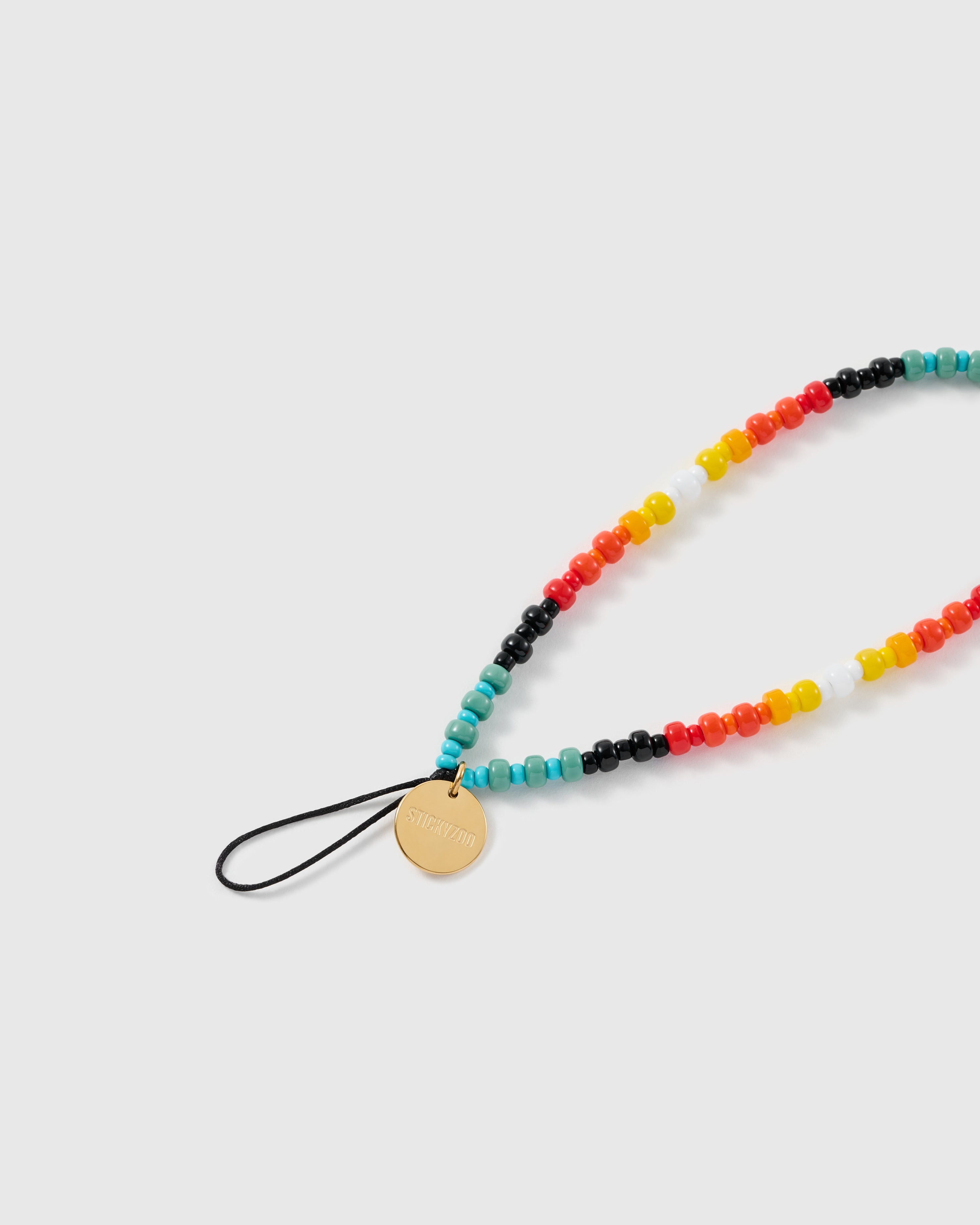 Close-up of the engraved gold-tone STICKYZOO disc and black stretch-cord loop, with opaque pony beads in turquoise, red, orange, yellow and black.