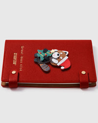 Red panda holiday charm detail showing hand-layered brown leather with Santa hat, green sweater, and striped tail on STICKYZOO A5 notebook
