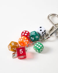 Close-up of red, green, orange, amber, and white polyhedral gaming dice on stainless steel chain with mini heart padlock charm and carabiner clasp