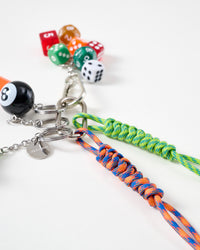 Close-up of blue-orange and green hand-braided paracord ropes with STICKYZOO engraved stainless steel tag, 8-ball charm, and colorful dice cluster