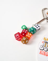 Close-up of red, green, orange, amber, and white translucent polyhedral gaming dice on stainless steel chain with carabiner clasp and Bee Kind tag