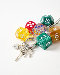 Dice and heart lock detail | Close-up of translucent yellow, red, green, and amber polyhedral gaming dice with silver heart padlock and ornate skeleton keys on stainless steel chain