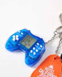 Macro close-up of translucent blue mini arcade game controller with LCD screen, white buttons, music and rotate controls, connected to stainless steel chain
