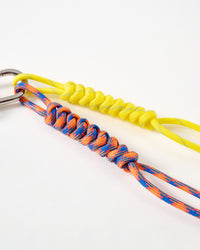 Close-up of yellow and blue-orange hand-knotted paracord ropes with intricate braiding pattern connected to stainless steel carabiner clasp