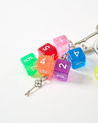 Rainbow translucent dice | Macro close-up of seven translucent numbered dice in green, orange, red, pink, purple, blue, and yellow with white numbers and silver clover key charm on chain