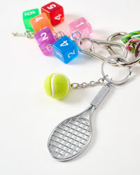 Tennis racket and rainbow dice | Close-up of silver mini tennis racket with felt tennis ball and translucent rainbow dice in blue, purple, pink, green, orange, and red on stainless steel chain