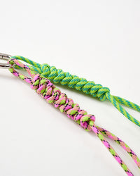 Stainless steel hardware | Close-up of neon green and pink-purple hand-braided paracord ropes with intricate knotting pattern connected to stainless steel carabiner clasp