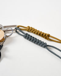Hand-braided paracord ropes | Close-up of charcoal black and mustard gold hand-knotted paracord ropes with intricate braiding pattern connected to stainless steel carabiner clasp