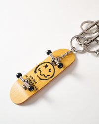 Wood fingerboard skateboard | Close-up of yellow real wood fingerboard deck with smiley face graphic, black trucks and wheels, connected to stainless steel chain and key rings