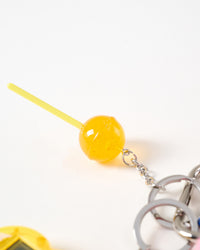 Glossy candy lollipop charm | Macro close-up of translucent orange-yellow glossy acrylic lollipop charm with sparkle effect on yellow stick connected to stainless steel chain and key rings