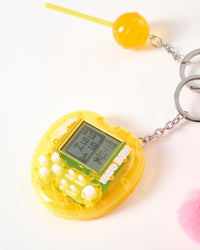 Yellow arcade game and lollipop | Close-up of translucent yellow mini arcade game with LCD screen and white buttons alongside glossy orange candy lollipop charm on stainless steel chain