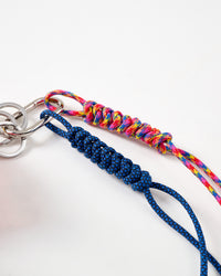 Rated 4.9 by thousands | Close-up of navy blue and rainbow multicolor hand-braided paracord ropes with intricate knotting pattern connected to stainless steel carabiner clasp and key rings