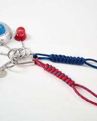 Hand-braided paracord ropes | Close-up of red and navy blue hand-knotted paracord ropes with intricate braiding pattern, stainless steel carabiner and key rings, with UFO saucer and red cap visible