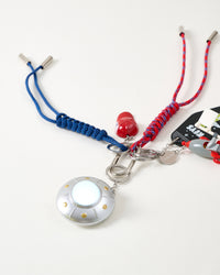 Rated 4.9 by thousands | Full spread of UFO Odyssey Stack Charm showing metallic flying saucer from above with glowing blue dome, red cap, stainless steel carabiner, and navy and red braided ropes with metal tips