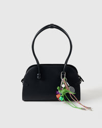 Clips onto any bag | Dino Stack Charm on black handbag showing green dinosaur, rainbow dice, tennis racket, and green and pink braided paracord ropes with stainless steel tips