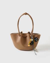 Clips onto any bag | Shadow Stack Charm on tan structured tote showing fingerboard deck, dark hero figure, mini game console, and black and mustard braided ropes