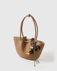 A detail people notice | Shadow Stack Charm on tan tote from three-quarter angle showing fingerboard, dark hero figure, game console, and black and mustard braided ropes with metal tips