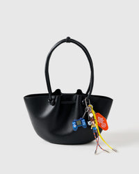 Arcade Cowboy Stack Charm clipped onto a black structured tote bag showing blue retro game controller, cowboy figure, 8-ball, orange motel tag, and yellow braided ropes