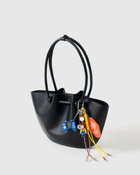 Arcade Cowboy Stack Charm on black tote from three-quarter angle showing game controller, cowboy figure, 8-ball, motel tag, and yellow and blue braided ropes with metal tips