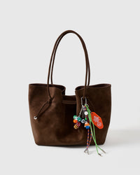 Lucky Roll Stack Charm clipped onto a dark brown suede tote bag showing colorful dice cluster, 8-ball, mini figure, orange motel tag, and green and blue braided ropes