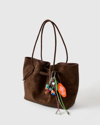 Lucky Roll Stack Charm on dark brown tote from side angle showing all charms including dice, 8-ball, character figure, motel tag, and colorful braided paracord ropes with metal tips