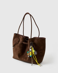 A detail people notice | Banana Rally Stack Charm on brown suede tote from side angle showing banana figure, tennis racket and ball, dice, and yellow braided ropes with stainless steel tips
