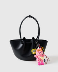 A detail people notice | STICKYZOO Poppy Stack Charm on black structured tote from front showing pink plush bunny, yellow arcade game, candy lollipop, and rainbow braided ropes with metal tips