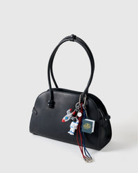Galactic Explorer Stack Charm on black handbag from three-quarter angle showing silver rocket, astronaut figure, 3D pop-up book, and red and navy braided ropes with metal tips
